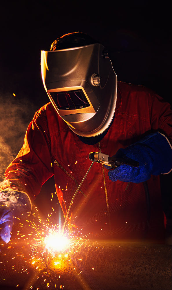 A welder in protective gear actively welding, creating a bright light and sparks.