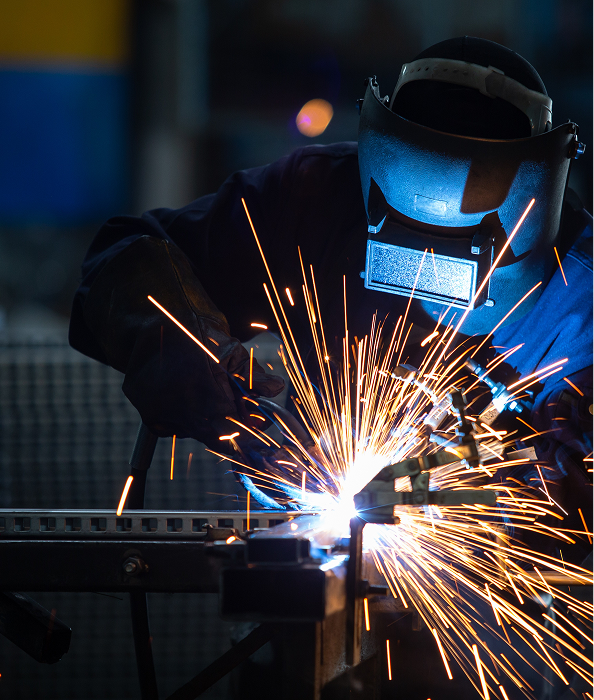A welder actively welding metal, creating a bright shower of sparks.